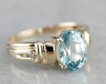 May include: A gold ring featuring a large oval blue gemstone and smaller diamonds set into the band.