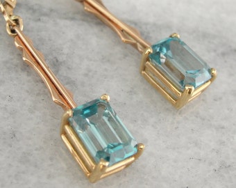 May include: Gold dangle earrings with blue topaz gemstones. The earrings have a delicate, vintage style.
