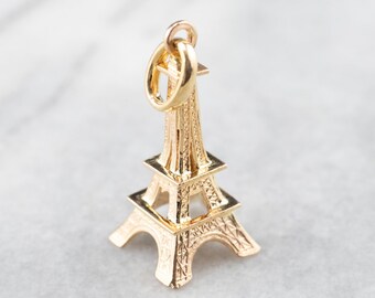 May include: Gold-toned Eiffel Tower charm pendant. The charm is detailed with intricate architectural features and has a loop at the top for attaching to a necklace or bracelet.
