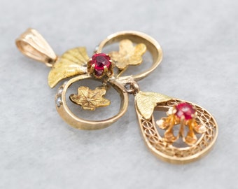 May include: A gold pendant with a delicate filigree design and two red gemstones. The pendant features a floral motif with leaves and a teardrop shape.