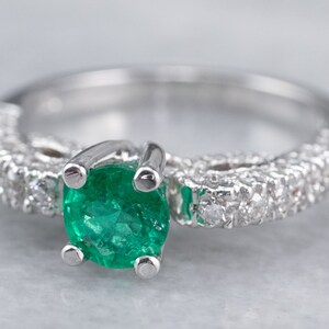 May include: A silver ring featuring a green emerald gemstone and a band of small diamonds.