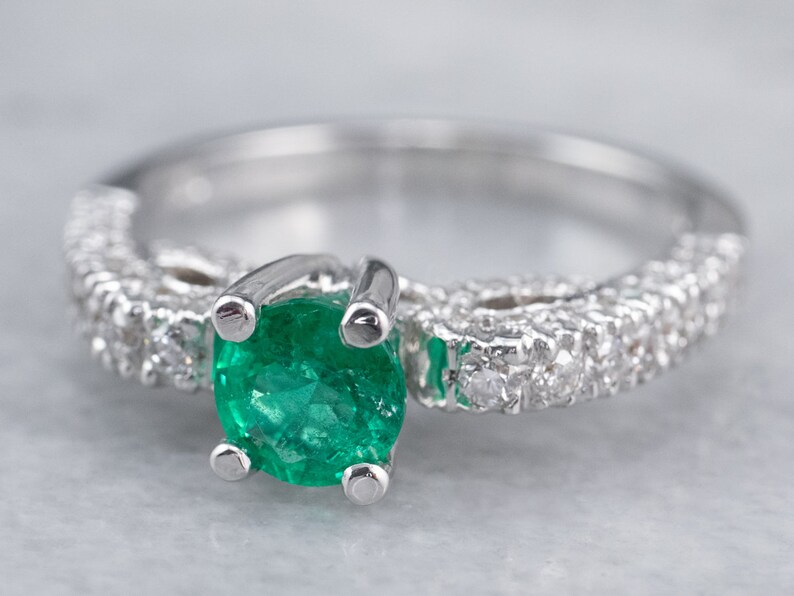 May include: A silver ring featuring a green emerald gemstone and a band of small diamonds.