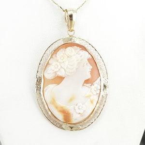 May include: A gold pendant with a cameo of a woman's profile carved from shell. The cameo is surrounded by a delicate gold filigree design.