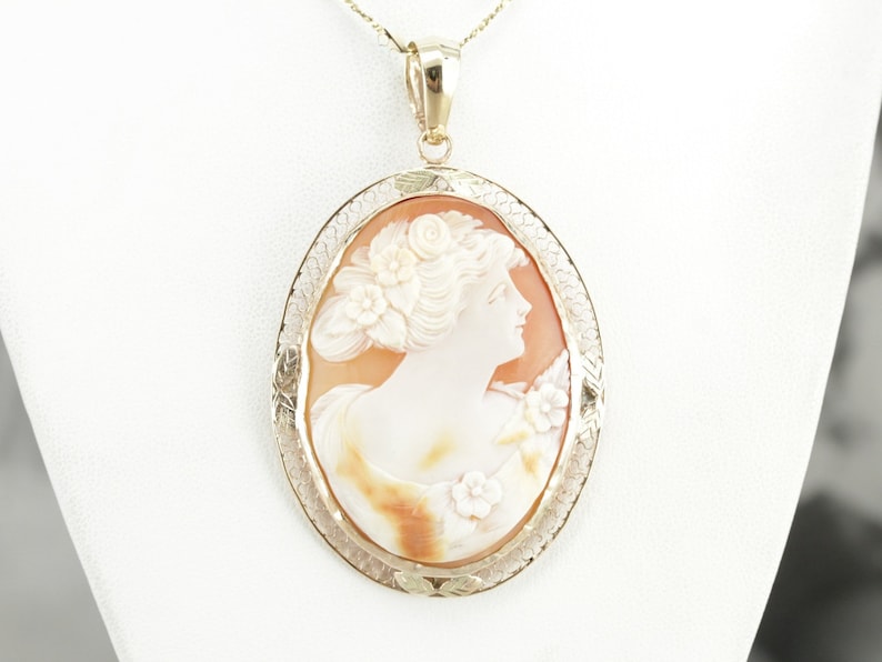 May include: A gold pendant with a cameo of a woman's profile carved from shell. The cameo is surrounded by a delicate gold filigree design.