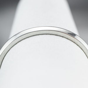 May include: A close-up of a silver ring with a smooth, polished finish. The ring is on a white display stand.
