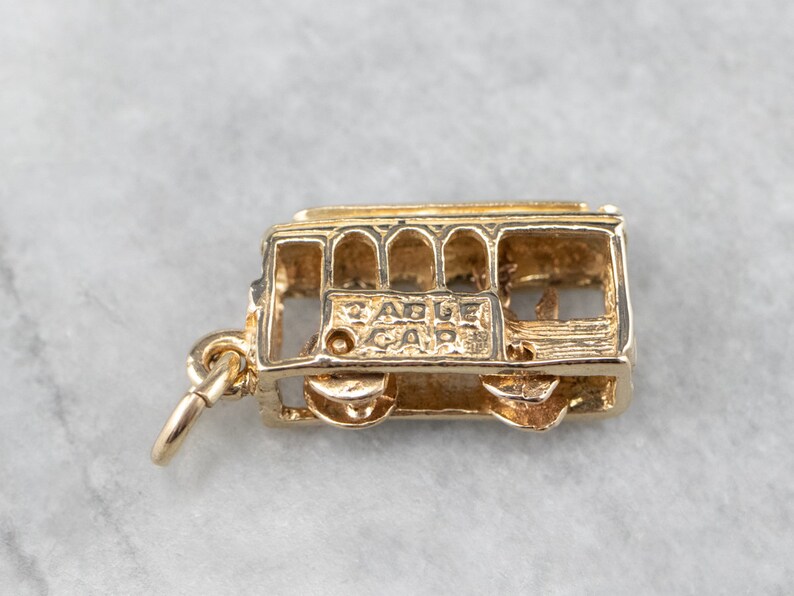 May include: Gold-tone charm of a San Francisco cable car. The charm has a detailed design and says "Cable Car" on the side.