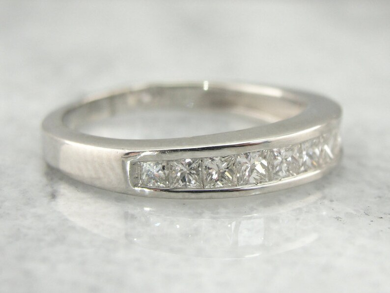 May include: A silver band ring with a row of small square-shaped diamonds set in a channel setting.