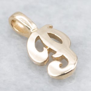 May include: A gold-colored pendant in the shape of the letter "P". The pendant has a loop at the top for a chain and a stylized, cursive design. The metal has a polished finish, reflecting light.