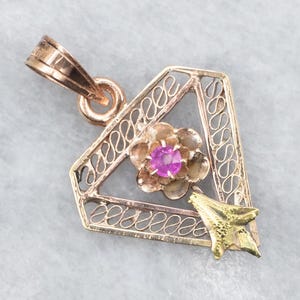 Puede incluir: Colgante vintage con diseño geométrico. El colgante presenta una flor central con una gema rosa y una estrella dorada. El marco es de color oro rosa con un diseño calado.