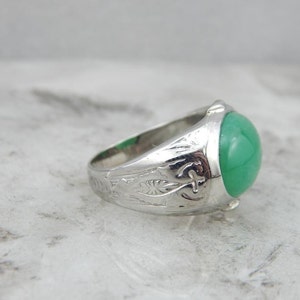 May include: A silver ring with an engraved band and a green gemstone. The ring is set in a cabochon style.