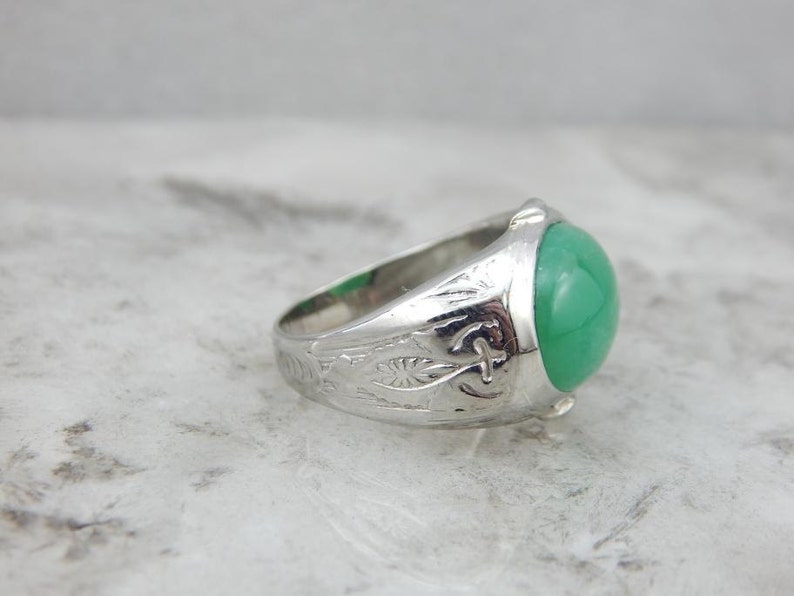 May include: A silver ring with an engraved band and a green gemstone. The ring is set in a cabochon style.