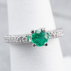 May include: A silver ring featuring a round emerald gemstone and a band of small diamonds.