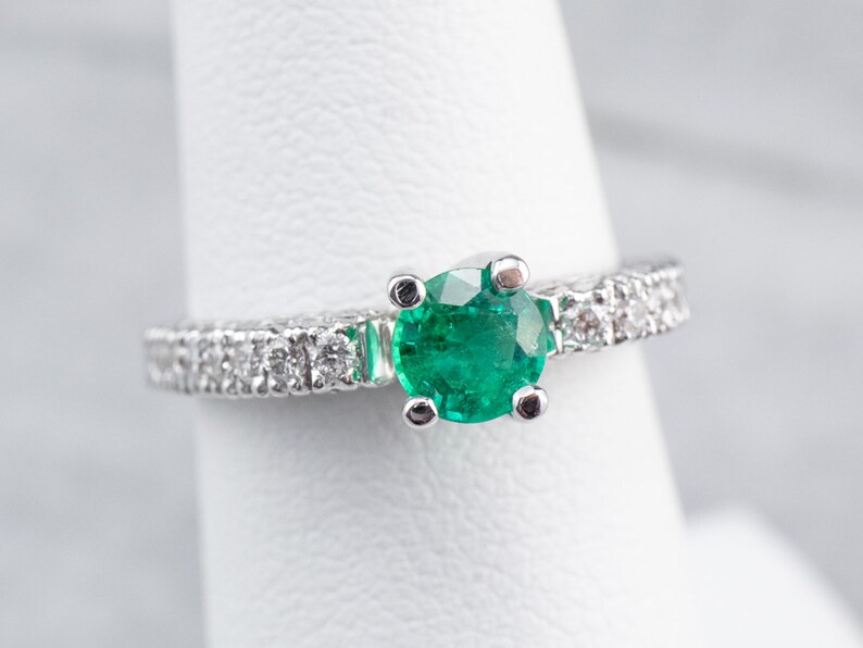 May include: A silver ring featuring a round emerald gemstone and a band of small diamonds.