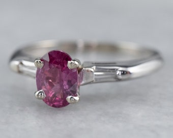 May include: A delicate silver ring with a pink oval gemstone set in a prong setting. The ring features two baguette-shaped diamonds on either side of the center stone.