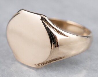 May include: A gold signet ring with a smooth, oval-shaped top. The ring has a slightly rounded band.