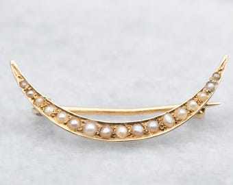 Op de afbeelding: Een halve maanvormige broche met een gouden zetting en een rij parels.