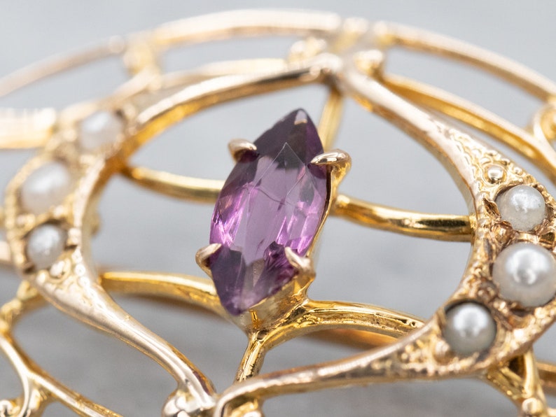 May include: A gold brooch with a purple gemstone and pearl accents. The brooch is in an intricate design with a delicate filigree pattern.