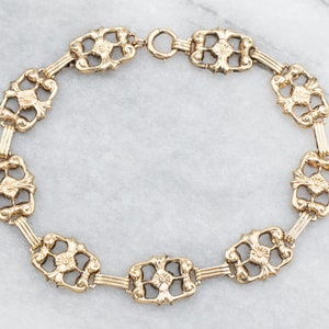 May include: A gold chain bracelet with a delicate, intricate design. Each link features a floral motif, creating a sophisticated and elegant look.