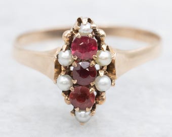 Könnte beinhalten: Ein goldener Ring mit einer Anordnung aus drei roten Edelsteinen und sechs kleinen weißen Perlen. Der Ring hat ein schlichtes Goldband, und die Edelsteine sind in einer dekorativen Goldeinfassung gefasst.