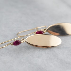 Puede incluir: Un par de pendientes de oro con colgantes de forma ovalada y detalles de piedras preciosas rojas.