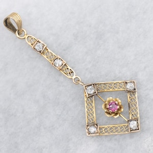May include: A gold pendant with a square filigree design, featuring four clear gemstones at the corners and a pink gemstone flower in the centre. The pendant has a rectangular top with three clear gemstones.