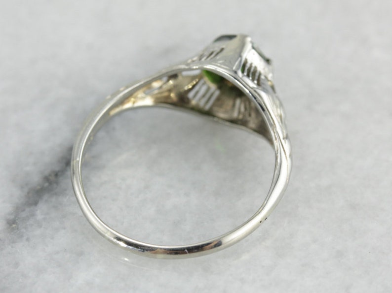 May include: A silver ring with a green gemstone set in a filigree design.