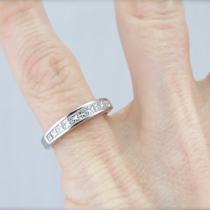 May include: A silver band ring with a row of small, square-shaped diamonds.