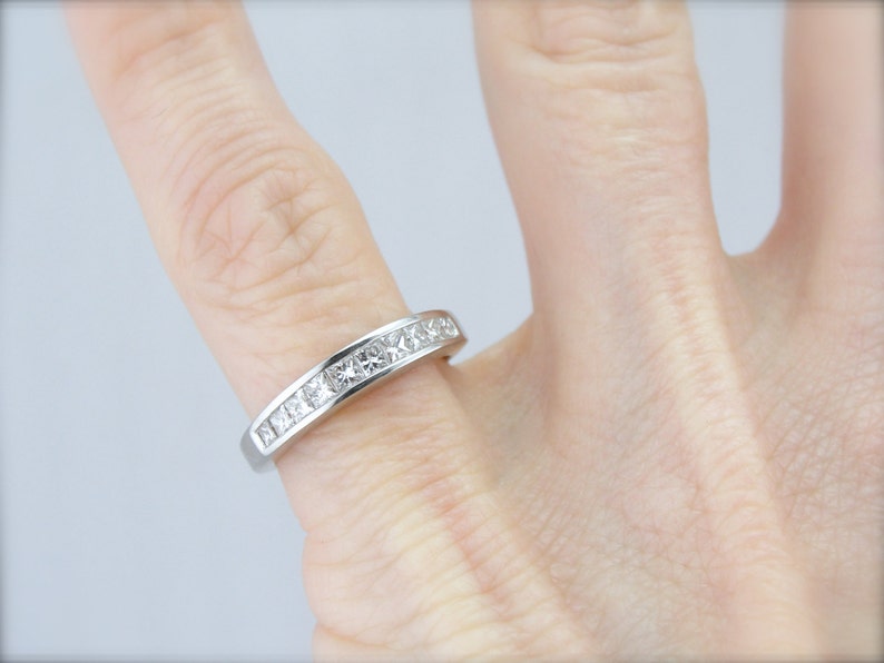 May include: A silver band ring with a row of small, square-shaped diamonds.