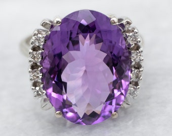 May include: A large oval amethyst gemstone ring set in white gold with a halo of smaller diamonds.