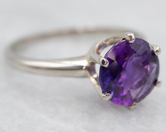 May include: A silver ring featuring a large, round, purple amethyst gemstone set in a claw setting.