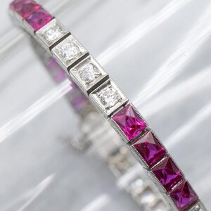 May include: A silver bracelet featuring alternating square-cut rubies and round diamonds. The rubies are a deep pink color, and the diamonds sparkle. The bracelet is set in a silver metal with a delicate design.