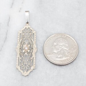 May include: A silver filigree pendant with a single diamond in the center. The pendant is about the size of a US quarter.