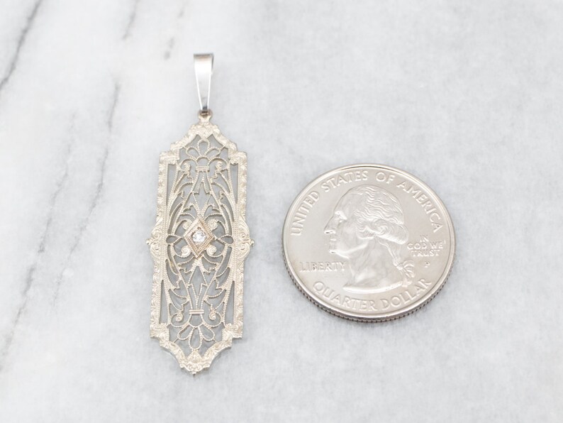 May include: A silver filigree pendant with a single diamond in the center. The pendant is about the size of a US quarter.
