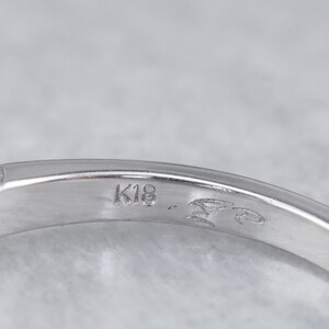 May include: Close-up of the inside of a silver ring with the inscription "K18" on the band.