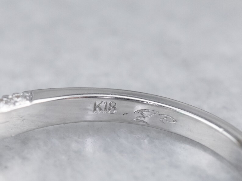 May include: Close-up of the inside of a silver ring with the inscription "K18" on the band.