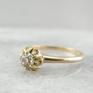Puede incluir: Un anillo de oro vintage con un diamante gris redondo y facetado engastado en un delicado engaste adornado.