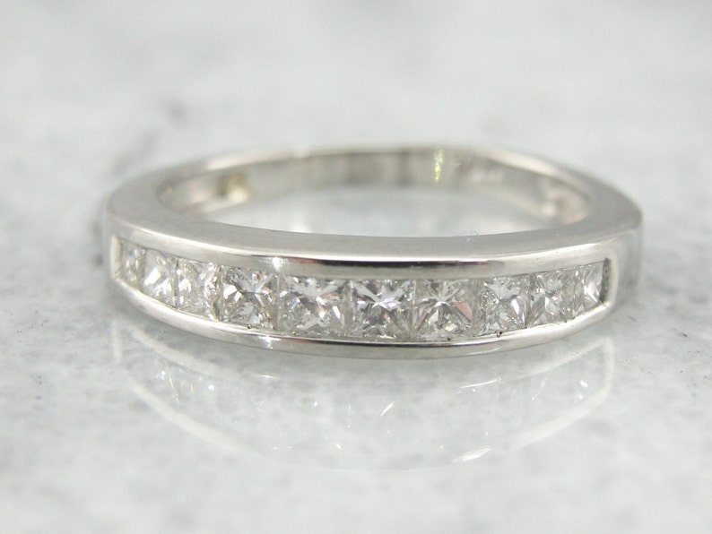 May include: A silver band with a row of square-shaped diamonds set in a channel setting.