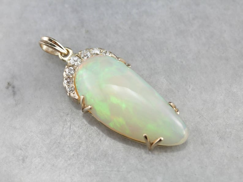 May include: A gold pendant featuring a large, oval-shaped opal with a green and white iridescent sheen. The opal is surrounded by a halo of small, sparkling diamonds.