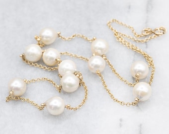 Puede incluir: Un collar dorado con grandes perlas blancas cremosas. Las perlas están espaciadas a lo largo de una delicada cadena dorada. El collar se muestra sobre una superficie clara, contrastando las perlas y la cadena. Aproximadamente 40 cm de largo.