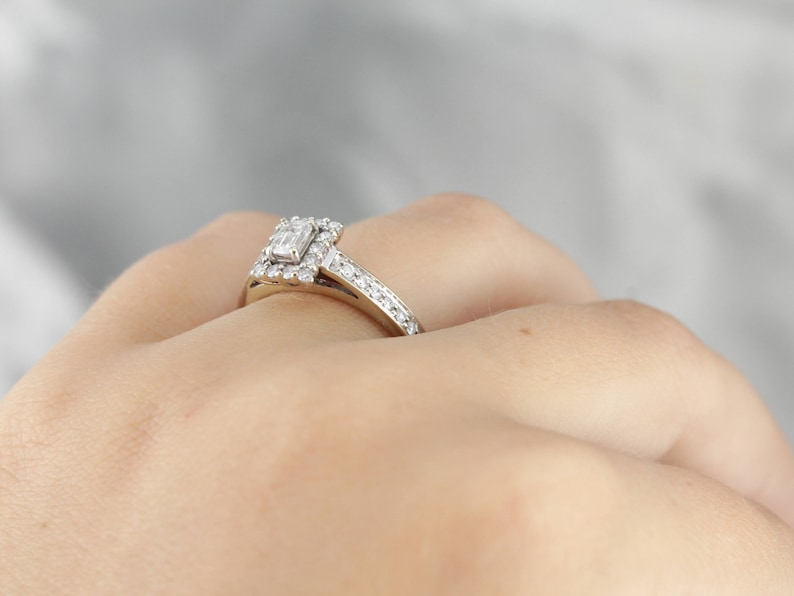 Puede incluir: Un anillo de compromiso de plata con un diamante central de forma cuadrada rodeado de diamantes m&aacute;s peque&ntilde;os. La banda tambi&eacute;n est&aacute; engastada con diamantes m&aacute;s peque&ntilde;os.