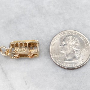 May include: Gold charm of a San Francisco cable car. The charm is about the size of a US quarter.