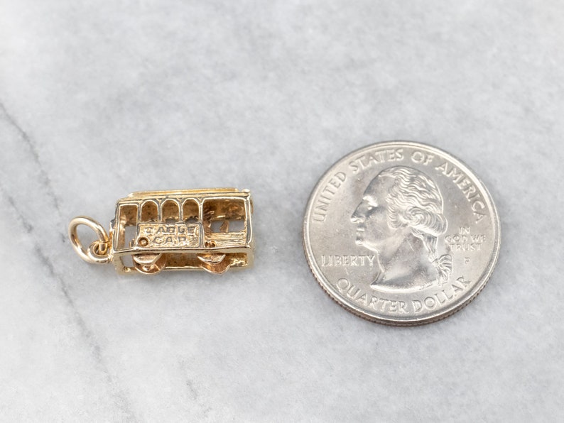 May include: Gold charm of a San Francisco cable car. The charm is about the size of a US quarter.