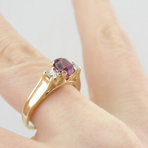 May include: A gold ring with a large oval purple gemstone and two smaller round white gemstones.