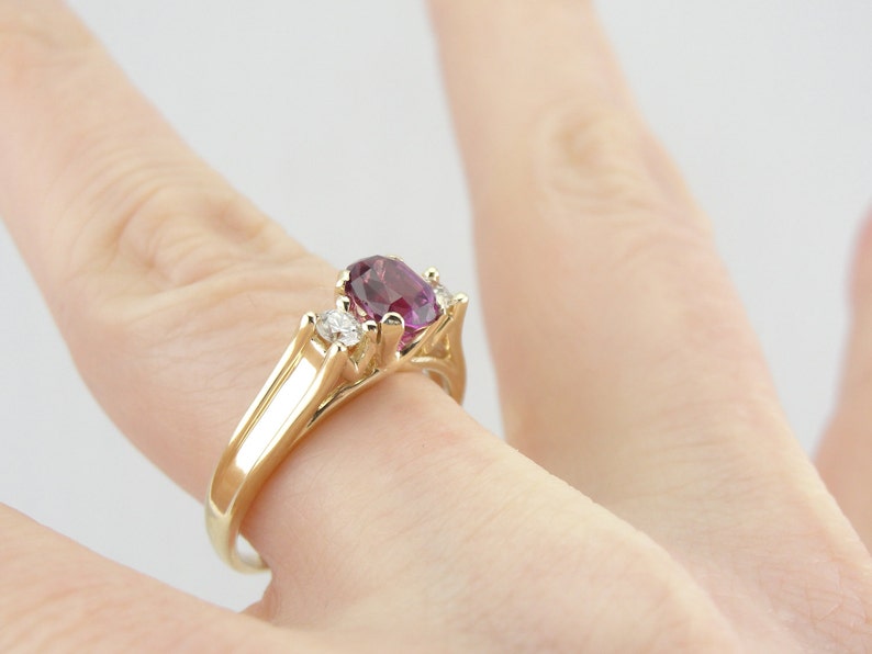 May include: A gold ring with a large oval purple gemstone and two smaller round white gemstones.