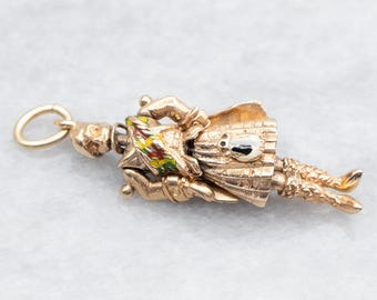 May include: A gold charm pendant depicting a figure in a colorful costume. The figure is wearing a hat and holding a staff. The charm has a loop for attaching to a chain or bracelet.