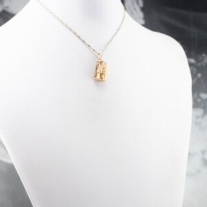 May include: A gold chain necklace with a gold pendant. The pendant is a geometric design with a textured surface.