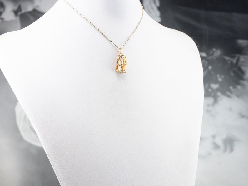 May include: A gold chain necklace with a gold pendant. The pendant is a geometric design with a textured surface.
