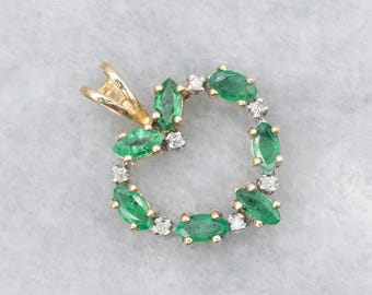 Puede incluir: Colgante de oro con un diseño circular de esmeraldas y diamantes. Las esmeraldas son ovaladas y verdes, mientras que los diamantes son pequeños y claros. El colgante tiene una fianza de oro para sujetarlo a una cadena.