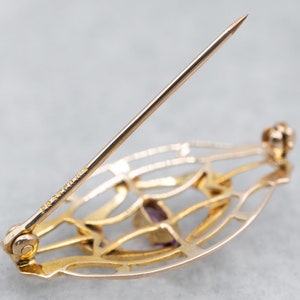 May include: A gold-toned brooch with a delicate, openwork design featuring a purple gemstone. The brooch has a pin and catch closure.