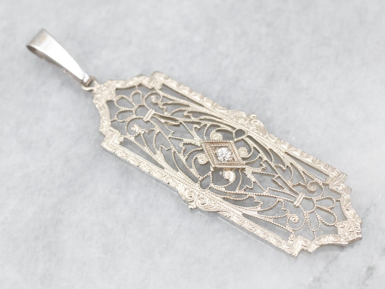 May include: A delicate silver pendant with an intricate filigree design and a single diamond in the center.